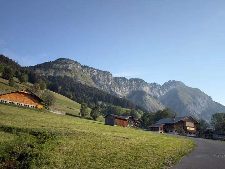 The full Mont Chauffé ridge stretching above green fields and wooden chalets, from wooded slopes to jagged limestone cliffs.