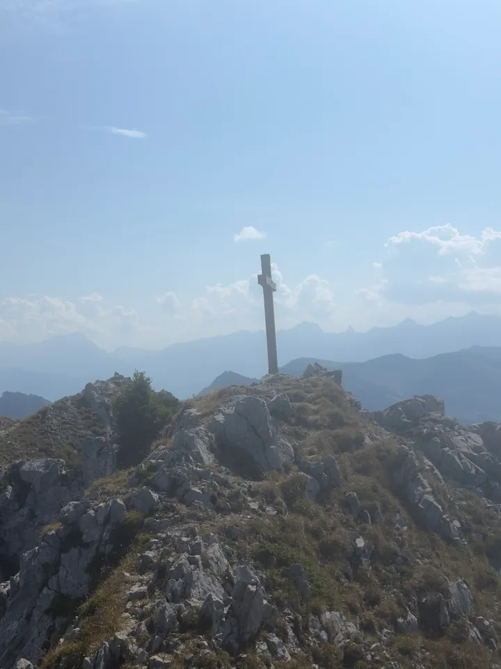 A cross on the rocky summit, with mountain ranges in the distance.
