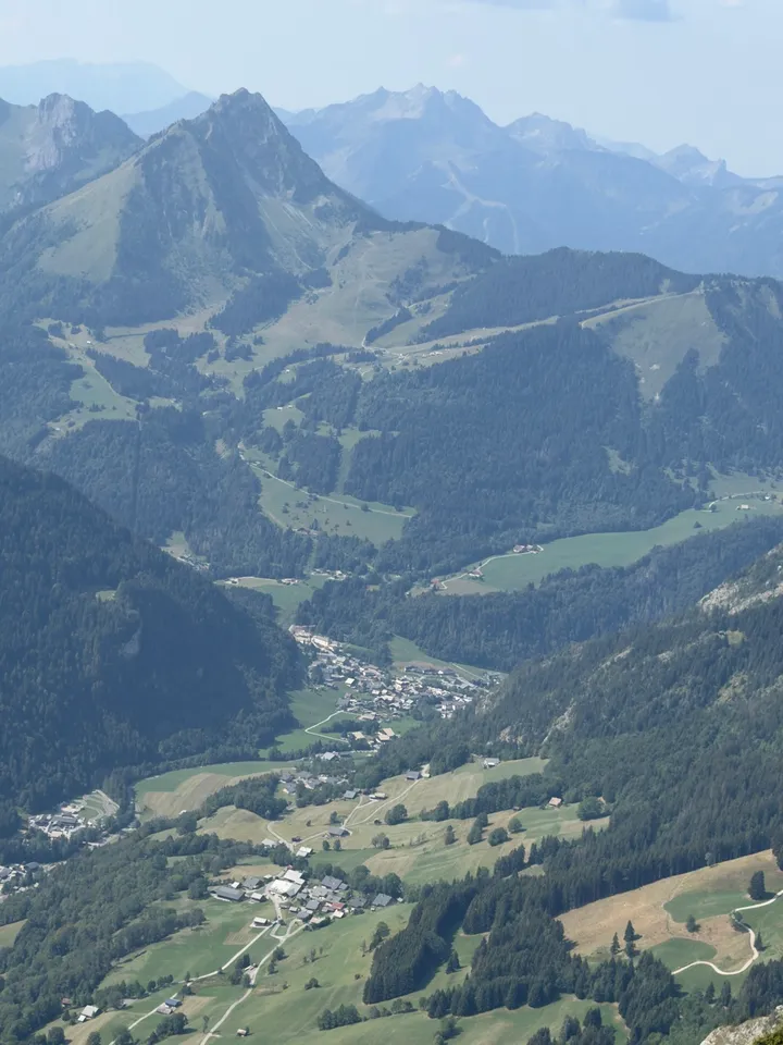 A view across the valley, with houses, green slopes and mountain peaks.